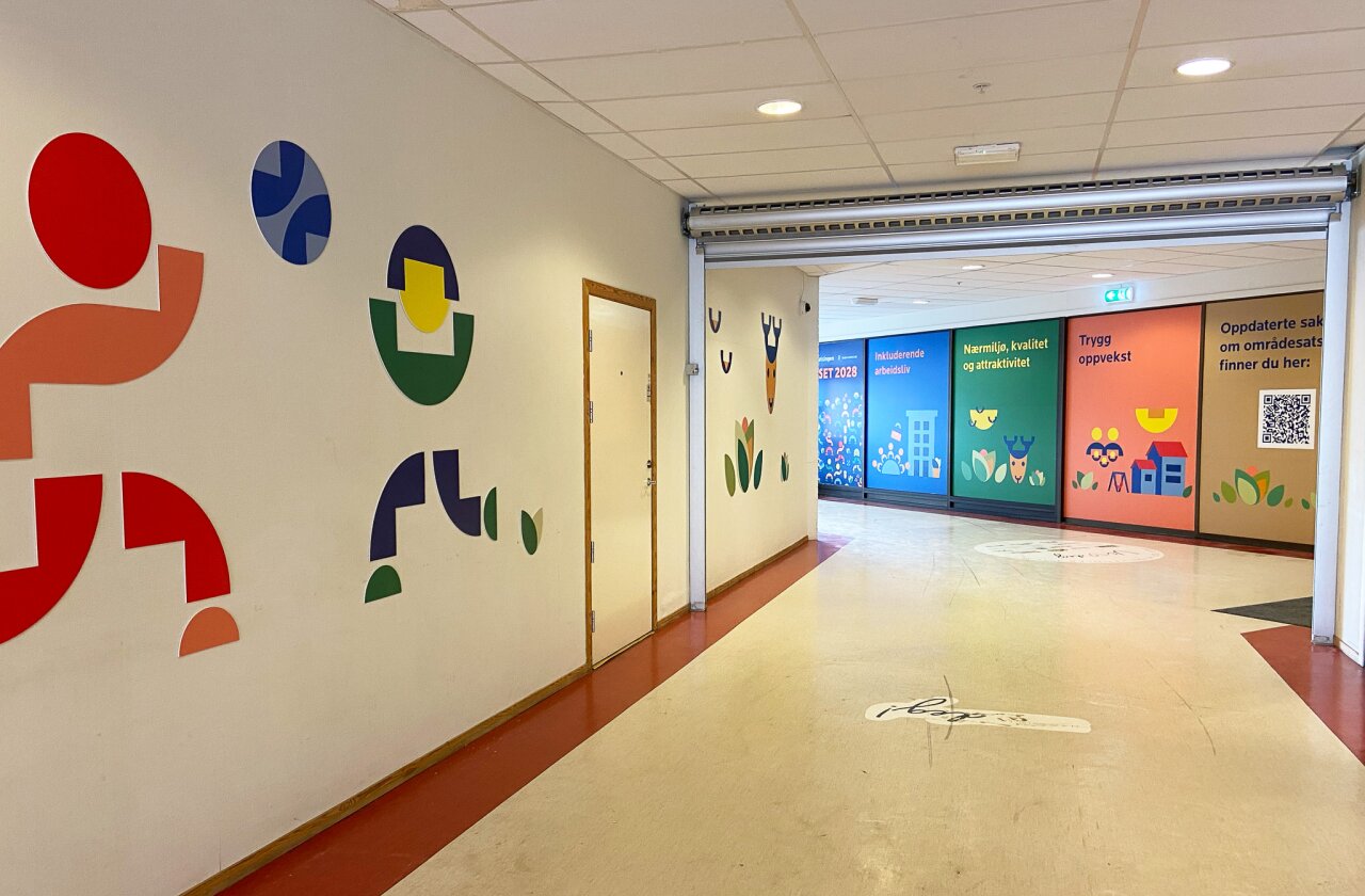 En gang med dekor av figurer på venstre vegg, og helfolierte, fargerike vegger med sitater til høyre.