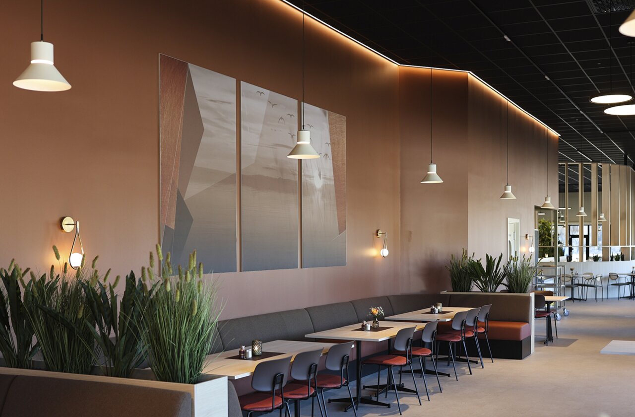 Kaféomgivelser med spisegrupper, veggdekor, grønne planter og belysning.