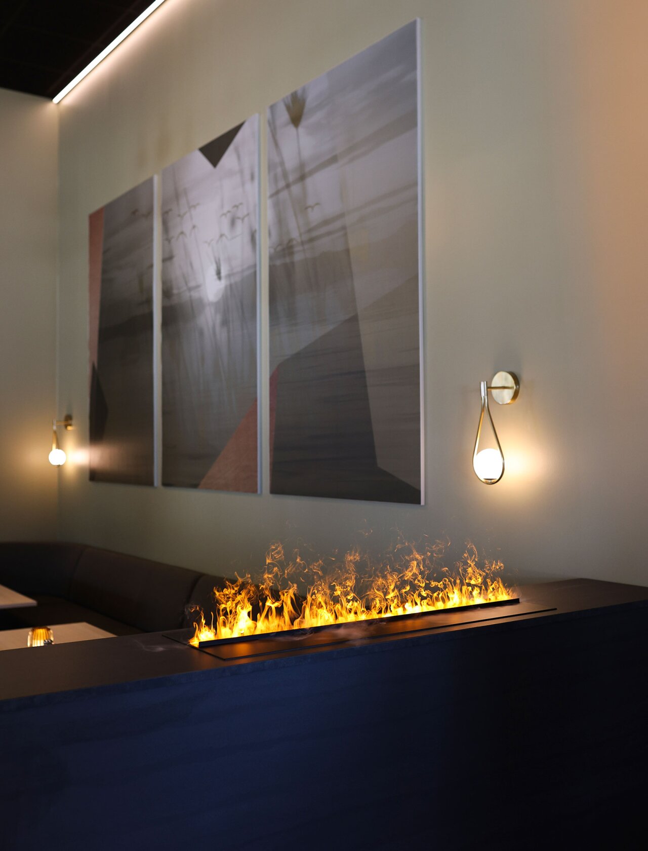 Et ildsted ved en sittegruppe, hvor man ser naturbilder henger på veggen i bakgrunnen.